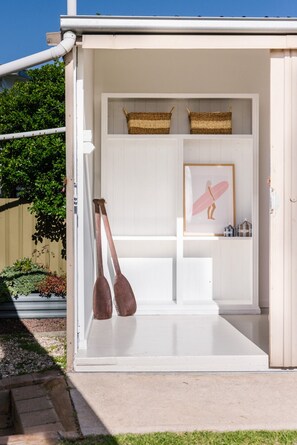 A white wooden structure with two wooden paddles leaning against it, a framed picture of a surfboard, and two woven baskets on shelves. - Champagne Beach | Sleeps 10 | Pet Friendly (Goolwa Beach)