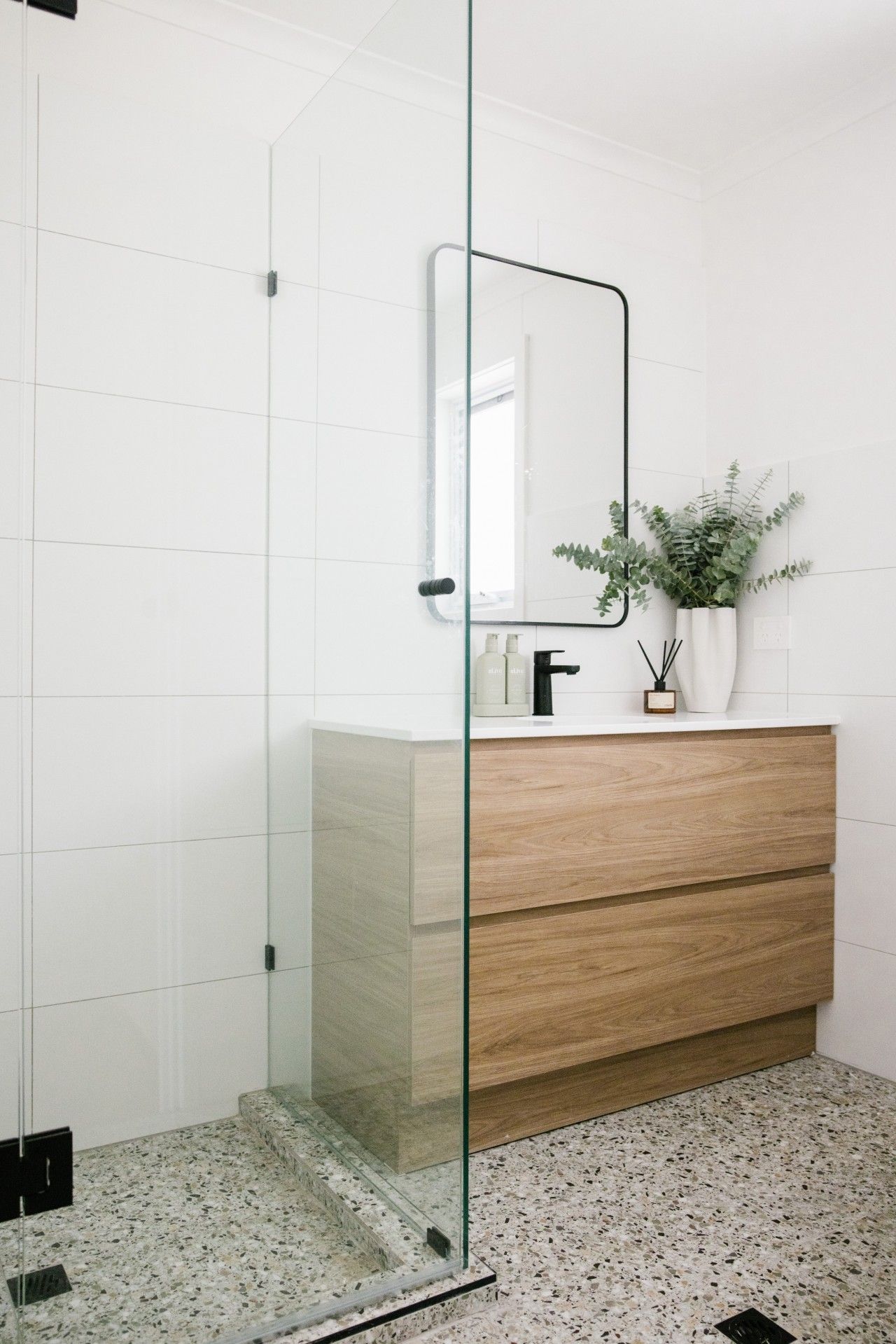 A modern bathroom with a glass shower enclosure, a wooden vanity, and a mirror.