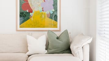 A living room with a beige sofa, a framed abstract painting, and a window with blinds.