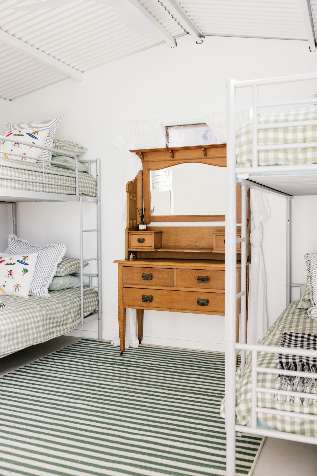 A dormitory room with bunk beds, a wooden dresser with drawers, and a striped floor.
