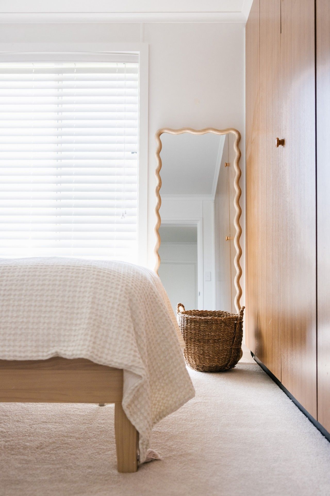 A bedroom with a bed, a wooden wardrobe, a mirror, and a wicker basket.