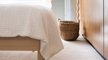 A bedroom with a bed, a wooden wardrobe, a mirror, and a wicker basket.
