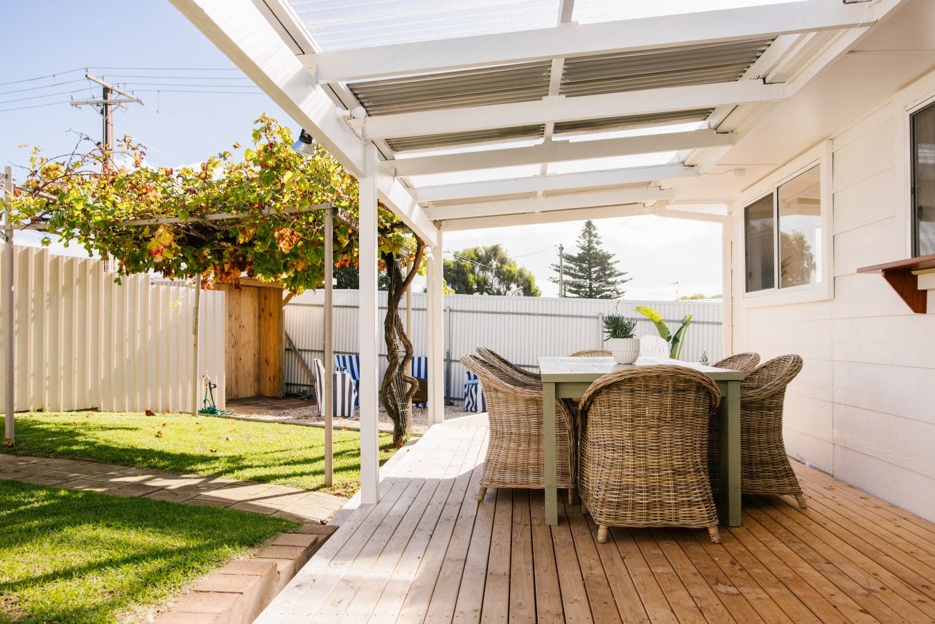 Un patio techado con una mesa y sillas, una terraza de madera y una valla blanca.