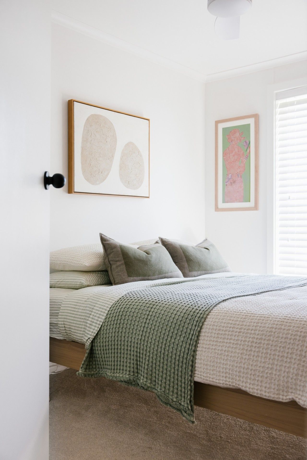 A bedroom with a bed, pillows, a blanket, and two framed artworks on the wall.