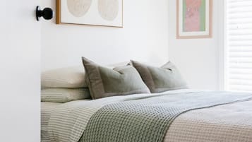 A bedroom with a bed, pillows, a blanket, and two framed artworks on the wall.