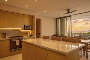 Una cucina moderna con isola centrale, elettrodomestici integrati e vista sull'oceano al tramonto.
