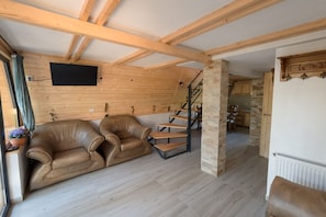 Un vaste espace de vie doté d’un plafond en bois, d’un canapé, d’un escalier et d’une cuisine en arrière-plan.