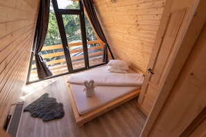 A bedroom with a wooden sloped ceiling, a bed with white bedding, a small rug, and a window with curtains. - Cabana Din Poiana, Poina Marului (Poiana Marului)