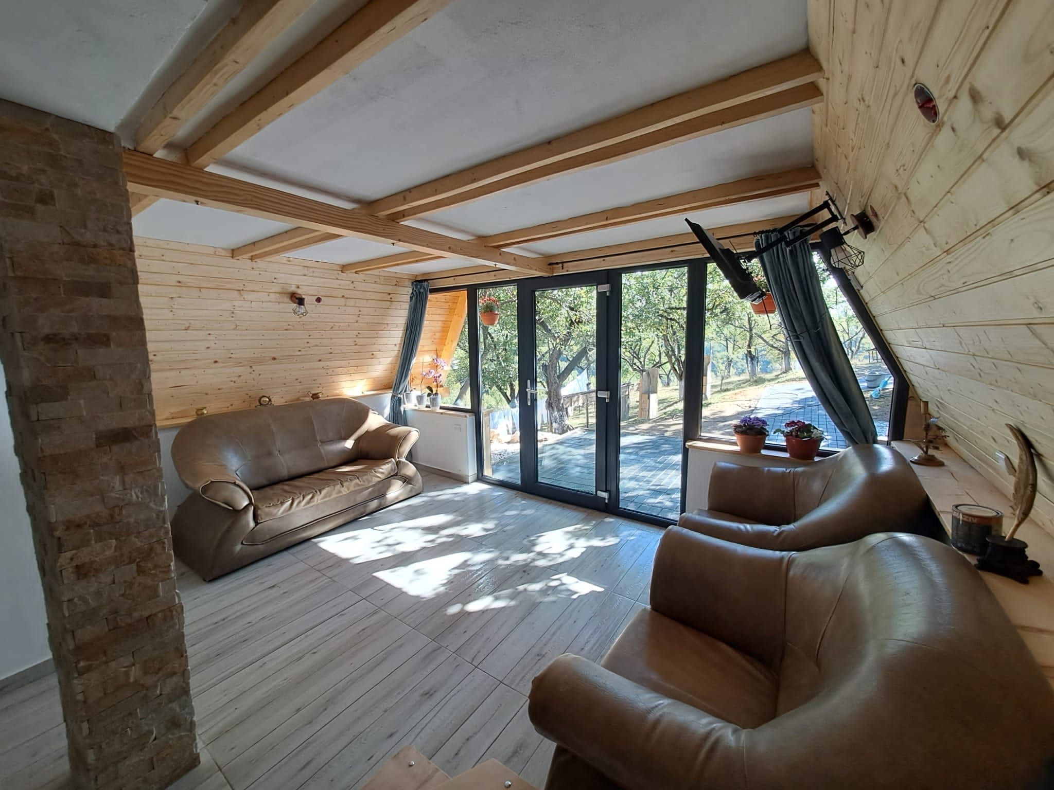 Une pièce spacieuse dotée d’une grande porte-fenêtre coulissante donnant sur un espace extérieur, d’un canapé en cuir marron et d’une structure de plafond en bois.