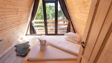 A small, cozy room with a wooden sloped ceiling, a single bed with white linens, a gray rug, and a window with curtains.