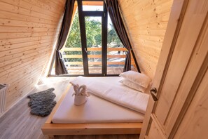 A small, cozy room with a wooden sloped ceiling, a single bed with white linens, a gray rug, and a window with curtains. - Cabana Din Poiana, Poina Marului (Poiana Marului)
