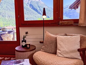 A cozy room with a wooden chair, a small table with a candle, and a view of mountains through a window. - Cozy Retreat near St. Moritz by Interhome (Madulain)