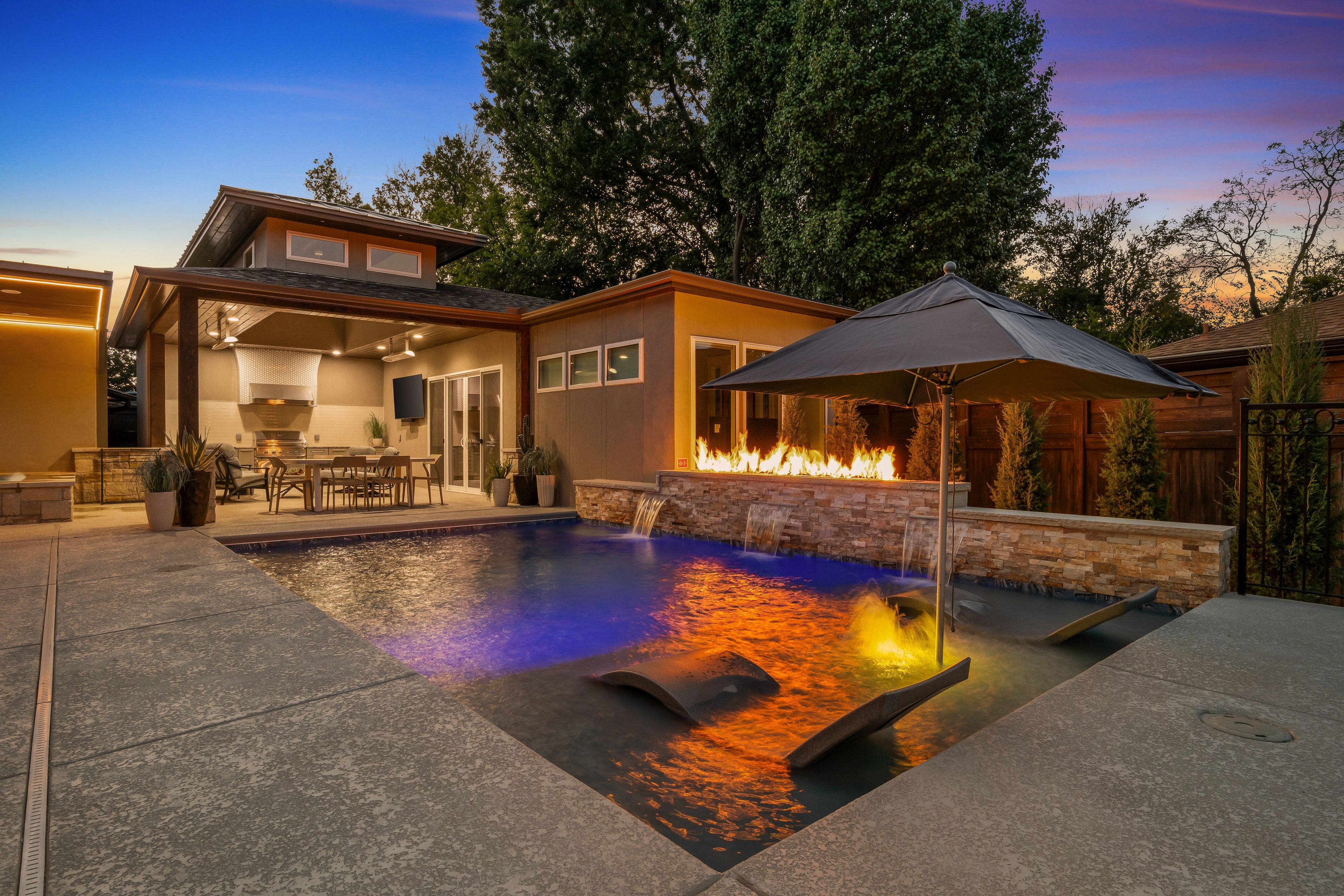 A backyard with a swimming pool, a fire feature, and a covered patio area.