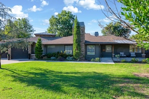 A two-story house with a stone chimney, a front porch, and a well-maintained lawn. - Modern Ranch Retreat | Pool, Hot Tub, Guest House (Tulsa)