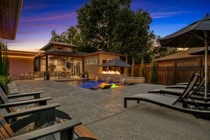 A backyard with a swimming pool, outdoor seating, and a fire feature. - Modern Ranch Retreat | Pool, Hot Tub, Guest House (Tulsa)