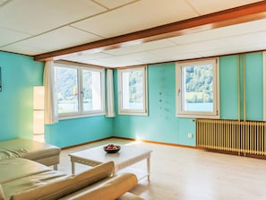 A room with a sofa, a table, and a view of a lake through large windows. - Ferienwohnung Enzian by Interhome (Lungern)