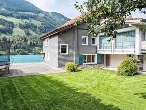 A two-story house with a swimming pool, a well-maintained lawn, and a view of the surrounding hills. - Ferienwohnung Enzian by Interhome (Lungern)