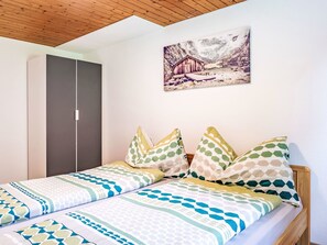 Une chambre avec deux lits, un plafond en bois, une armoire et un tableau au mur.