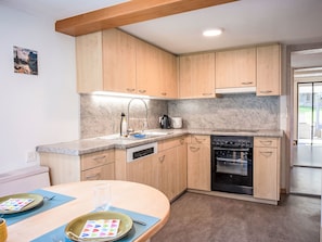 A modern kitchen with wooden cabinets, a granite countertop, a built-in oven, and a dining area with a table set for two. - Ferienwohnung Enzian by Interhome (Lungern)