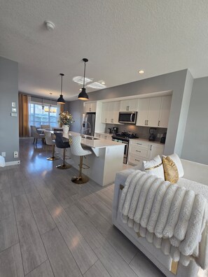 A modern kitchen with white cabinets, a central island, and stainless steel appliances. - Executive Home with Garage and Backyard - Near airport and park (Calgary)