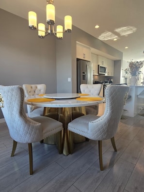 Een moderne eetruimte met een ronde tafel, gestoffeerde stoelen en een kroonluchter.