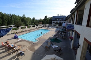 A swimming pool with lounge chairs and umbrellas, surrounded by a building with a balcony. - Celebrate the Holidays at Pollard Brook! (Lincoln)