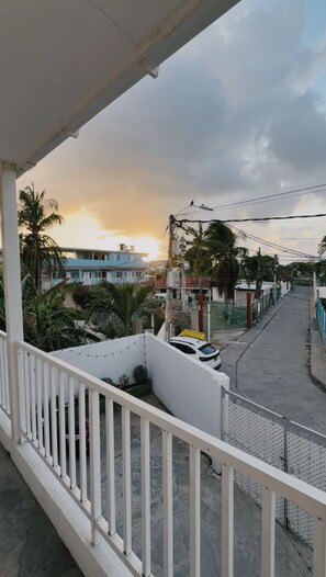 A balcony with a view of a street, palm trees, and a building with a blue facade. - Sariebay 3 Condo (San Andrés)