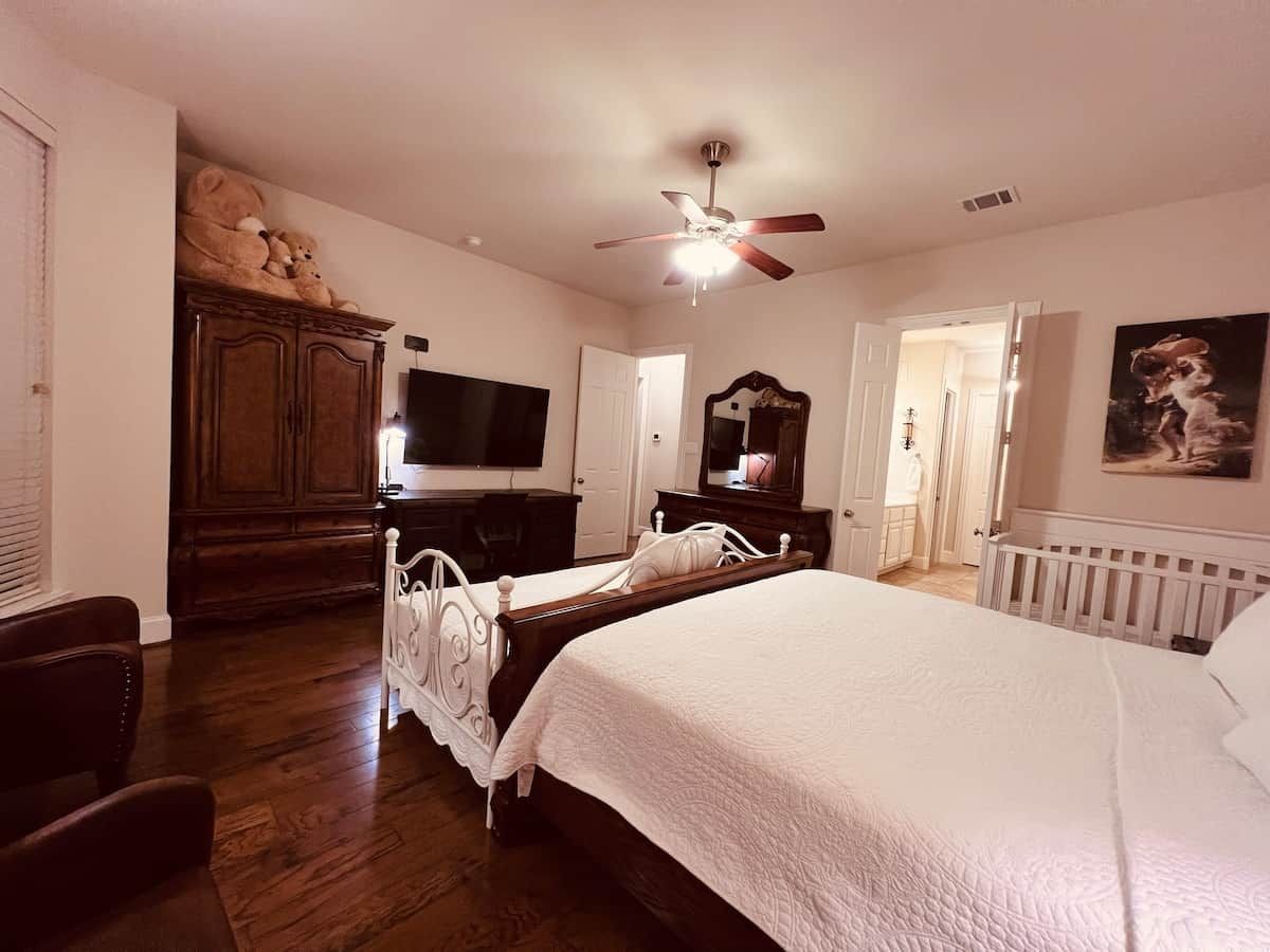 Un dormitorio con una cama grande, un armario de madera, un televisor y un ventilador de techo.