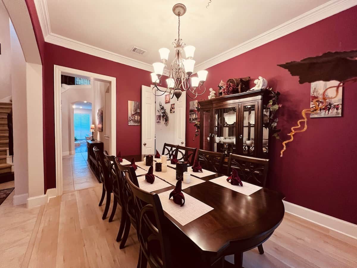 Een eetkamer met een donker houten tafel voor zes personen, een kroonluchter en een rode accentmuur.