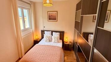 A bedroom with a bed, bedside lamps, a window, a wall-mounted artwork, and a mirror.
