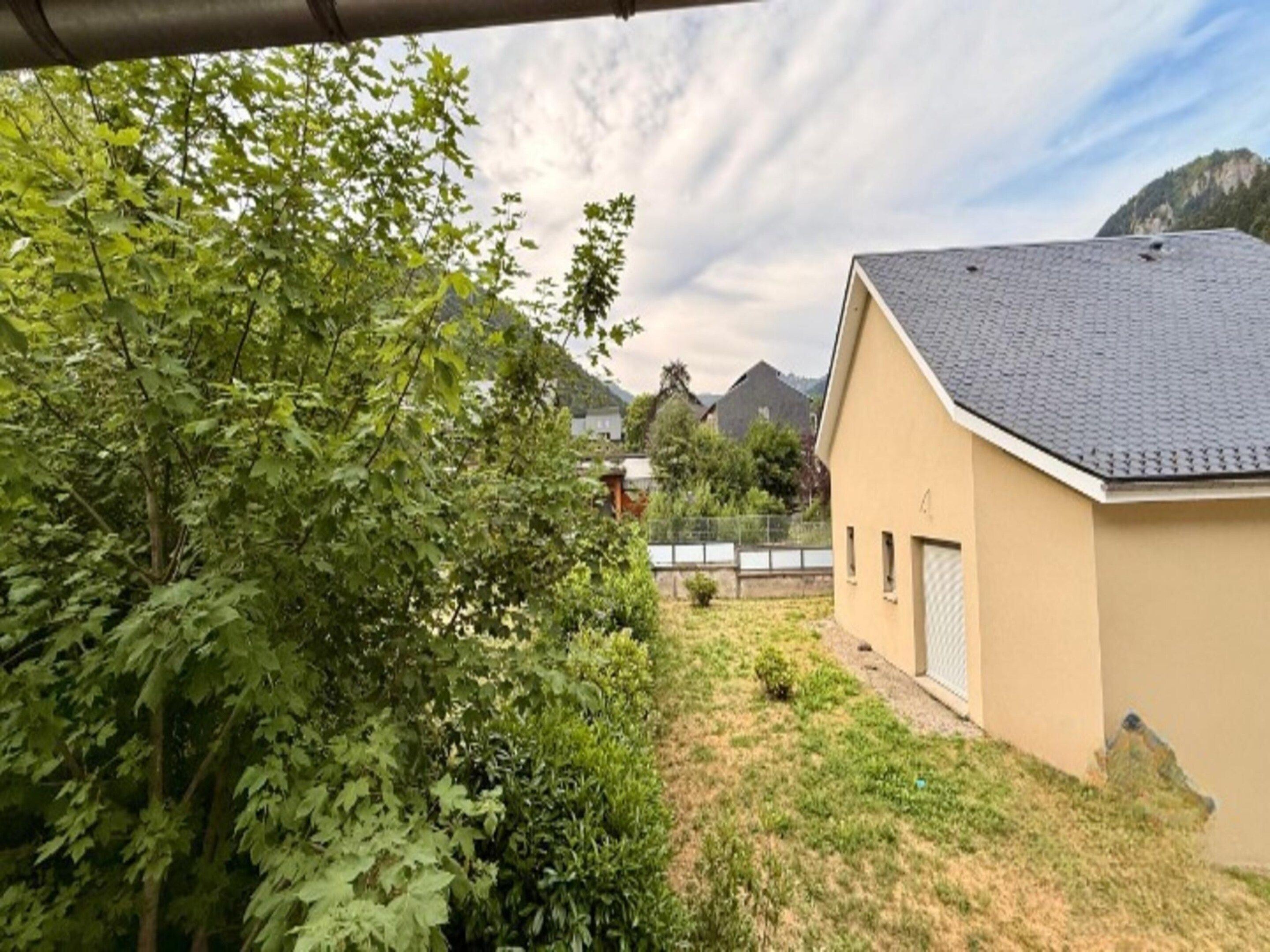 A residential building with a sloped roof, surrounded by dense foliage and a clear sky.