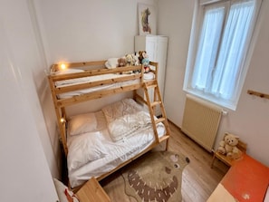 A bunk bed with a teddy bear on the top bunk, a radiator, and a window with curtains. - Family Apartment in Mont-dore (Mont-Dore)