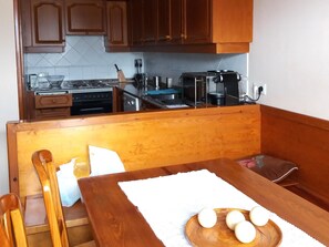 A kitchen with wooden cabinets, a stove, a sink, and a dining area with a table and chairs. - Apartment 3 rooms 8 Pax, Tennis, Fireplace, Views & Pet-Friendly (Ger)