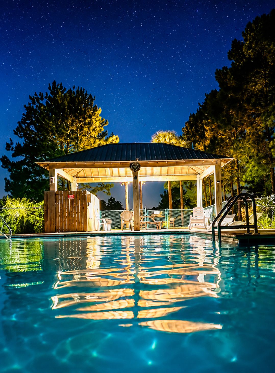 A swimming pool with a covered seating area and a view of the night sky.