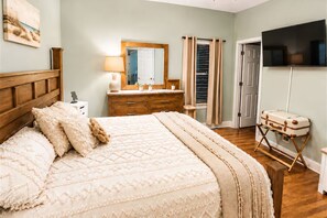 Een slaapkamer met een bed, een dressoir, een spiegel, een televisie en een koffer op een standaard.