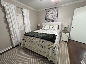 A bedroom with a bed, two bedside tables, a large floral artwork above the bed, and a door. - Quiet Waterfront Cabin, Private Dock, Fire Pit, Pet Friendly (Parsons)