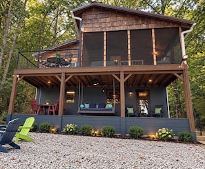 A two-story cabin with a covered porch, outdoor seating, and a view of the surrounding forest. - Quiet Waterfront Cabin, Private Dock, Fire Pit, Pet Friendly (Parsons)