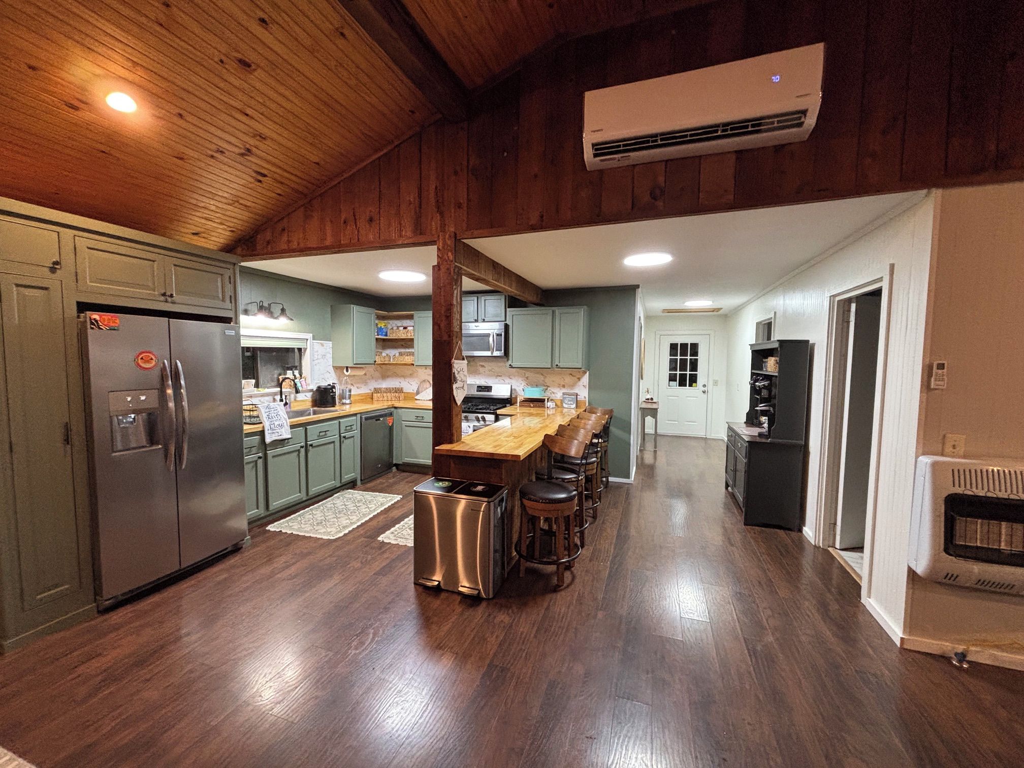 A modern kitchen with a central island, stainless steel appliances, and a wooden ceiling.