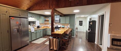A modern kitchen with a central island, stainless steel appliances, and a wooden ceiling.
