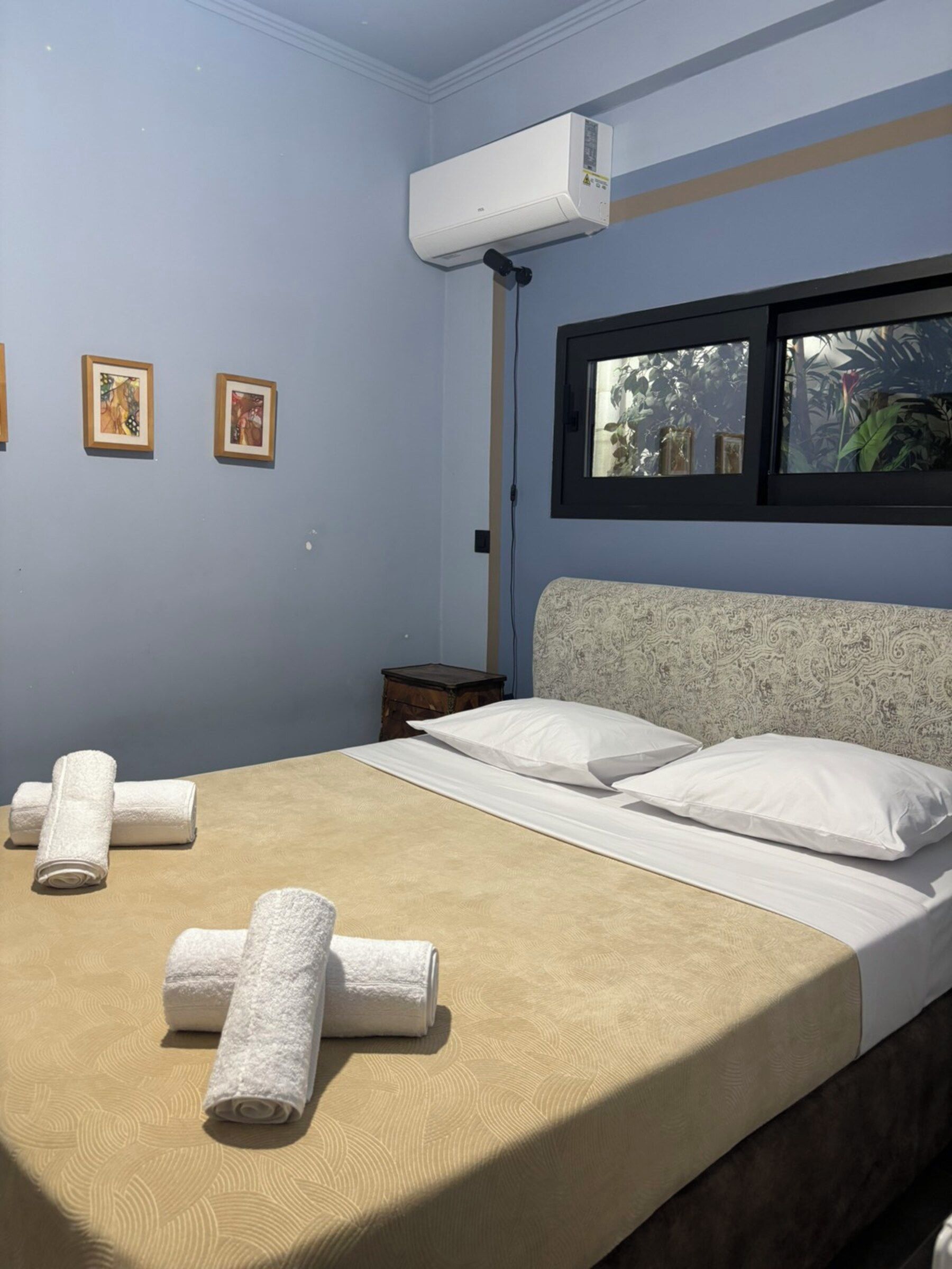 A hotel room with a bed, towels, a window with a view, and wall-mounted air conditioning.