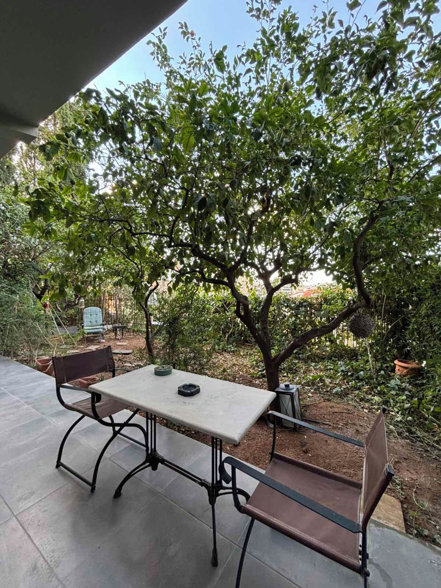 An outdoor patio with a table and chairs, surrounded by greenery and trees.