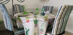 A dining table with a cactus-themed tablecloth, surrounded by striped chairs. - Flat With Pool Views in Corralejo (La Oliva)