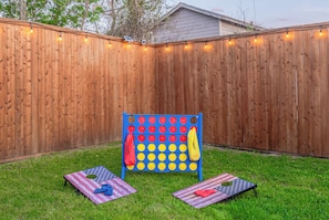 A backyard with a wooden fence, a blue and yellow game structure, and two American flag-themed mats. - Family & Friends Retreat, Hot Tub + Arcade + Cinema (Dallas)