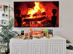 A room with a fireplace, a white cabinet with games, and a plant. - Family & Friends Retreat, Hot Tub + Arcade + Cinema (Dallas)