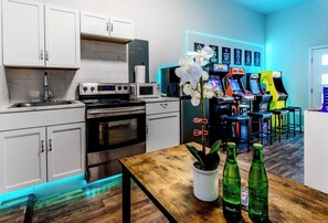 A modern kitchen with white cabinets, stainless steel appliances, and a wooden table with a potted plant and bottles. - Family & Friends Retreat, Hot Tub + Arcade + Cinema (Dallas)