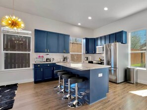 A modern kitchen with blue cabinets, stainless steel appliances, and a central island with bar stools. - Family & Friends Retreat, Hot Tub + Arcade + Cinema (Dallas)