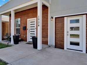A modern two-story house with a wooden facade, a garage door, and a front porch with chairs. - Family & Friends Retreat, Hot Tub + Arcade + Cinema (Dallas)
