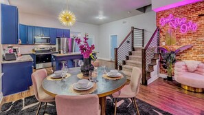 A modern kitchen with blue cabinets, a dining area with pink chairs, and a staircase with a neon sign. - Family & Friends Retreat, Hot Tub + Arcade + Cinema (Dallas)
