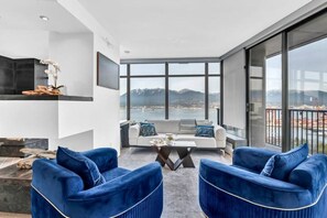 Un salon moderne comprenant un canapé, deux fauteuils, une table basse et une grande fenêtre donnant sur la ville.