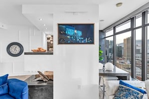 Un salon moderne avec vue sur la ville, un téléviseur encadré et une horloge au mur.